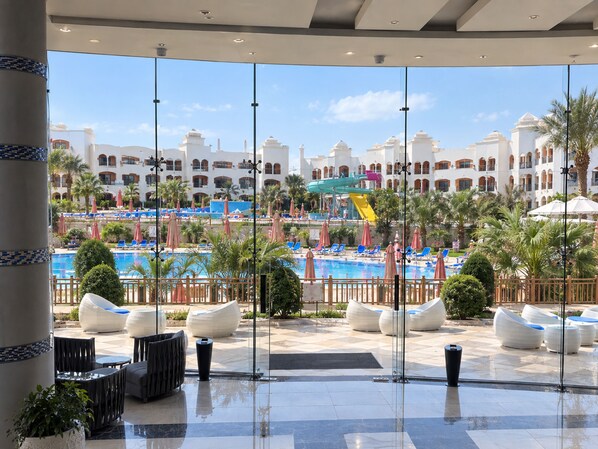 A hotel lobby with a large glass window overlooking a pool area, palm trees, and a water slide. - Naama Waves Hotel (Sharm El Sheikh)