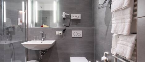 A modern bathroom with a glass-enclosed shower, a white sink, a toilet, and a towel rack with folded towels.