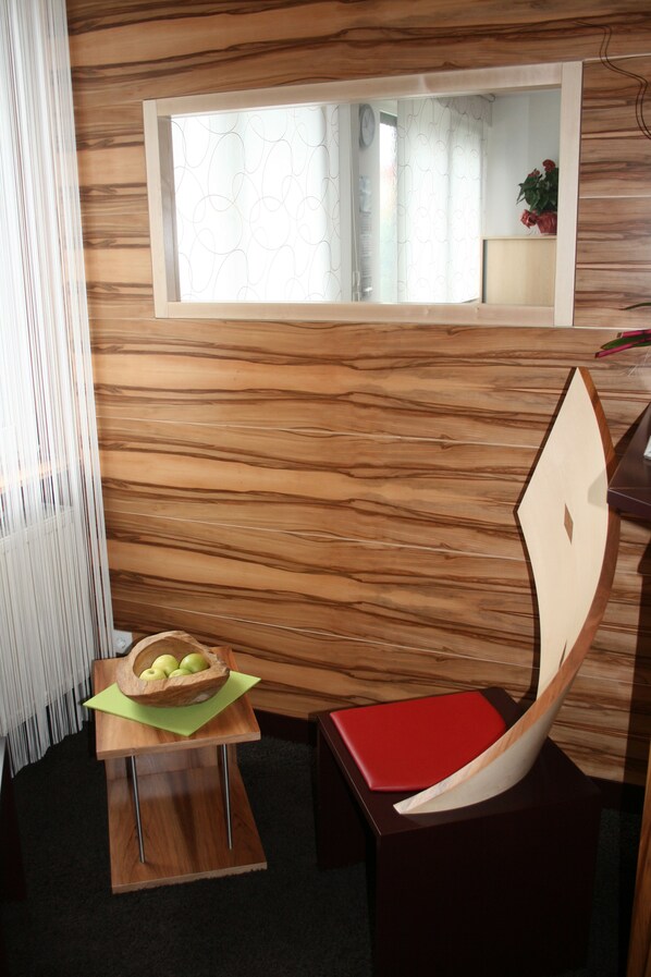 A modern room with a wooden wall, a small table with a bowl of apples, a red chair, and a window with a curtain.