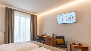 Quarto de hotel com cama, duas cadeiras, uma escrivaninha e uma mesinha.