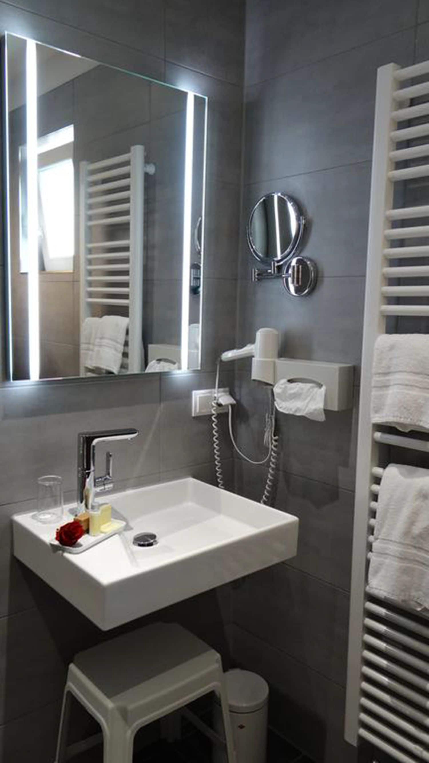 Un baño moderno con un lavamanos blanco, un espejo, un perchero para toallas y un secador de pelo.