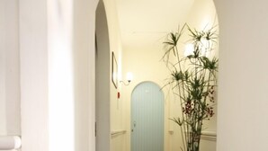 Un pasillo con suelo de baldosas, una planta grande en maceta y una puerta azul claro al final.
