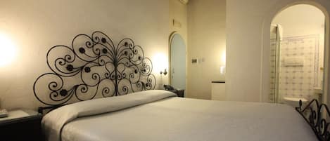 A bedroom with a bed, a nightstand, a decorative metal headboard, a bathroom with a shower and toilet visible through an archway.