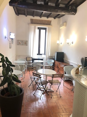 A dining area with white wicker furniture, a tiled floor, and a window with curtains. - Hotel Andreina (Rome)