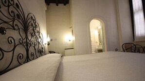 Una habitación de hotel con cama, mesita de noche, espejo y puerta hacia el baño.