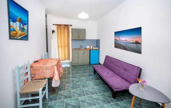 A compact living space with a dining table, a purple sofa, a small kitchen area, and a view of the sea.