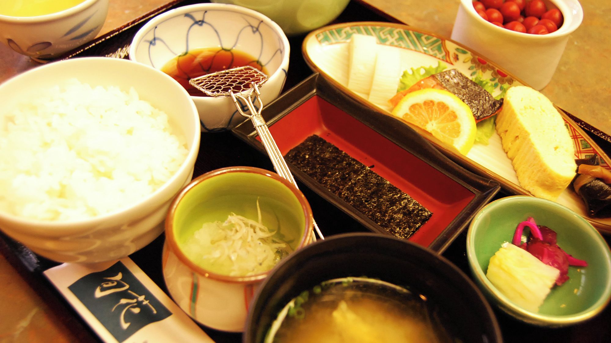 A traditional Japanese meal with rice, soup, and various dishes including fish, vegetables, and pickled items.