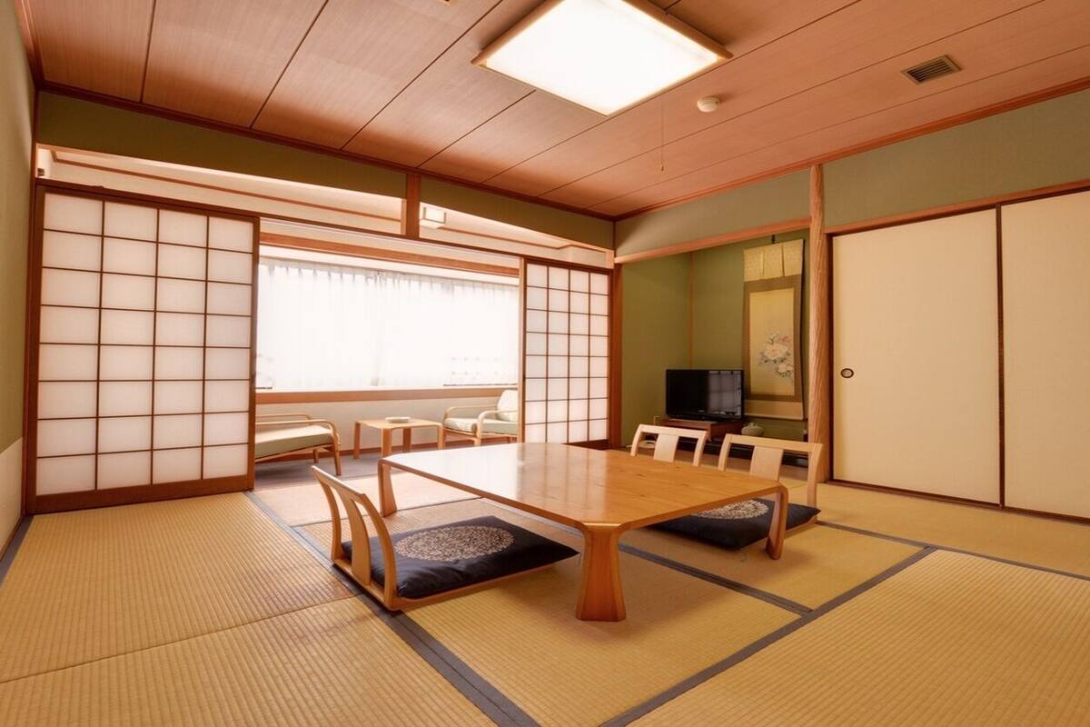 A traditional Japanese room with tatami flooring, a low table, sliding doors, and a television.