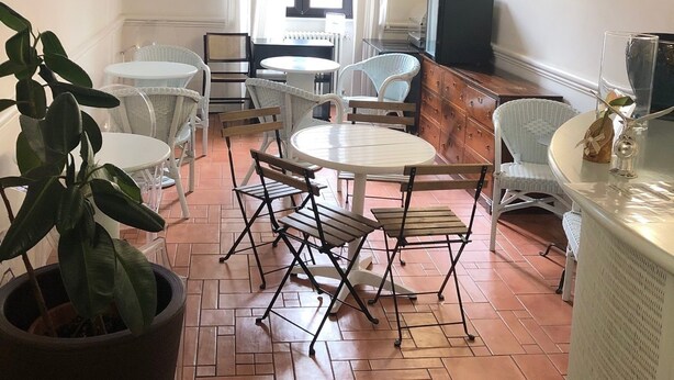 A dining area with white wicker furniture, a tiled floor, and a window with curtains. - Hotel Termini (Rome)