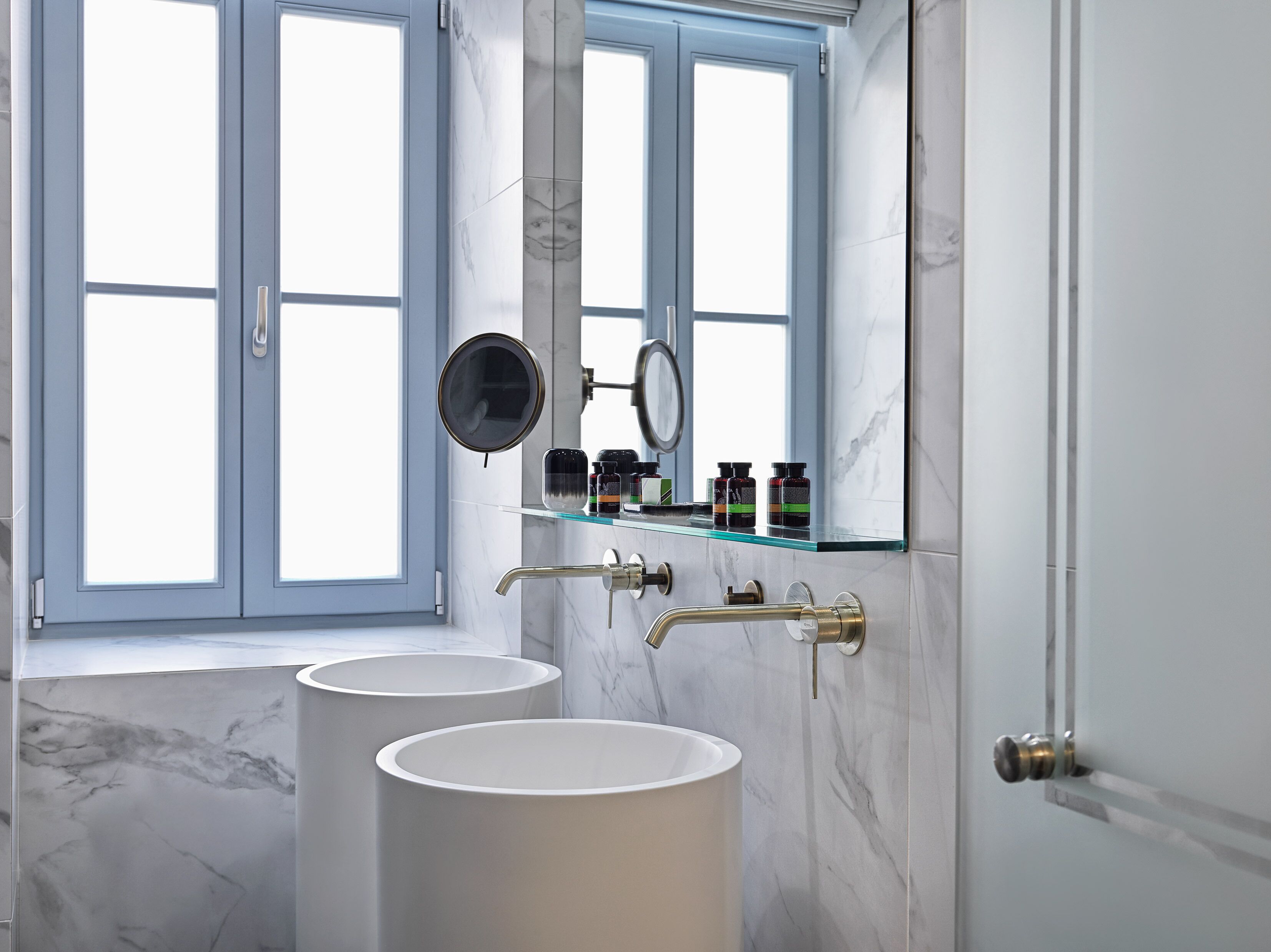A bathroom with two sinks, a mirror, and a shelf with toiletries.