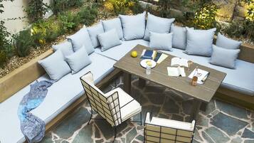 A stone patio with a curved seating area, a table, and chairs.