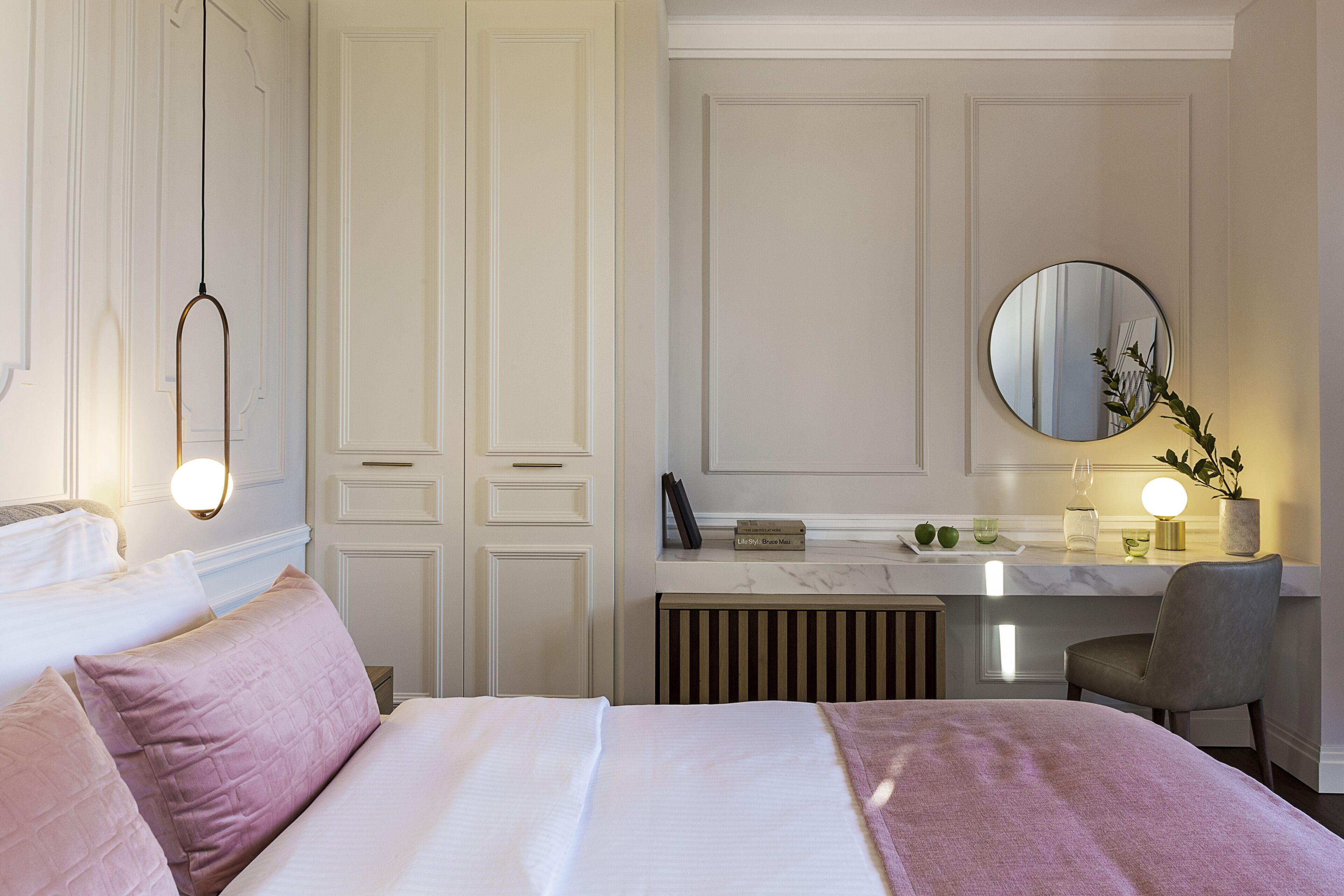 A hotel room with a bed, a desk, a chair, a mirror, and a radiator.