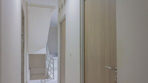 Un pasillo con una puerta de madera a la derecha, una pared blanca y una escalera al fondo.