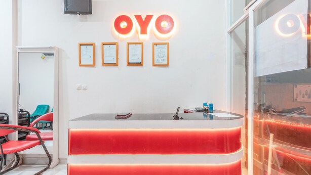 Una recepción con diseño rojo y blanco, televisor montado, certificados enmarcados y sillas rojas.