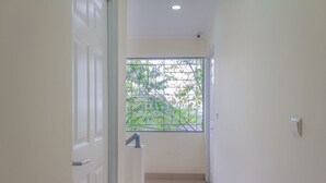 Un pasillo estrecho con una ventana al final, una puerta a la izquierda y un interruptor de luz a la derecha.