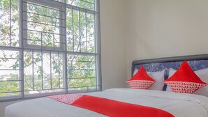 Una habitación de hotel con un ventanal grande, una cama con ropa blanca y detalles rojos, y almohadones decorativos.