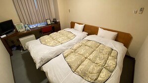 Een hotelkamer met twee bedden, een bureau met een computer en telefoon, en een televisie.