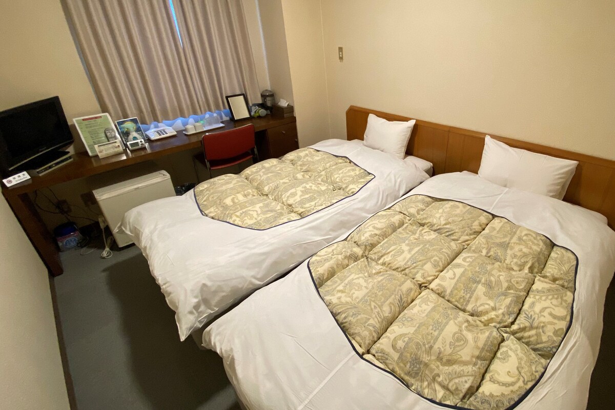 A hotel room with two beds, a desk with a computer and telephone, and a television.