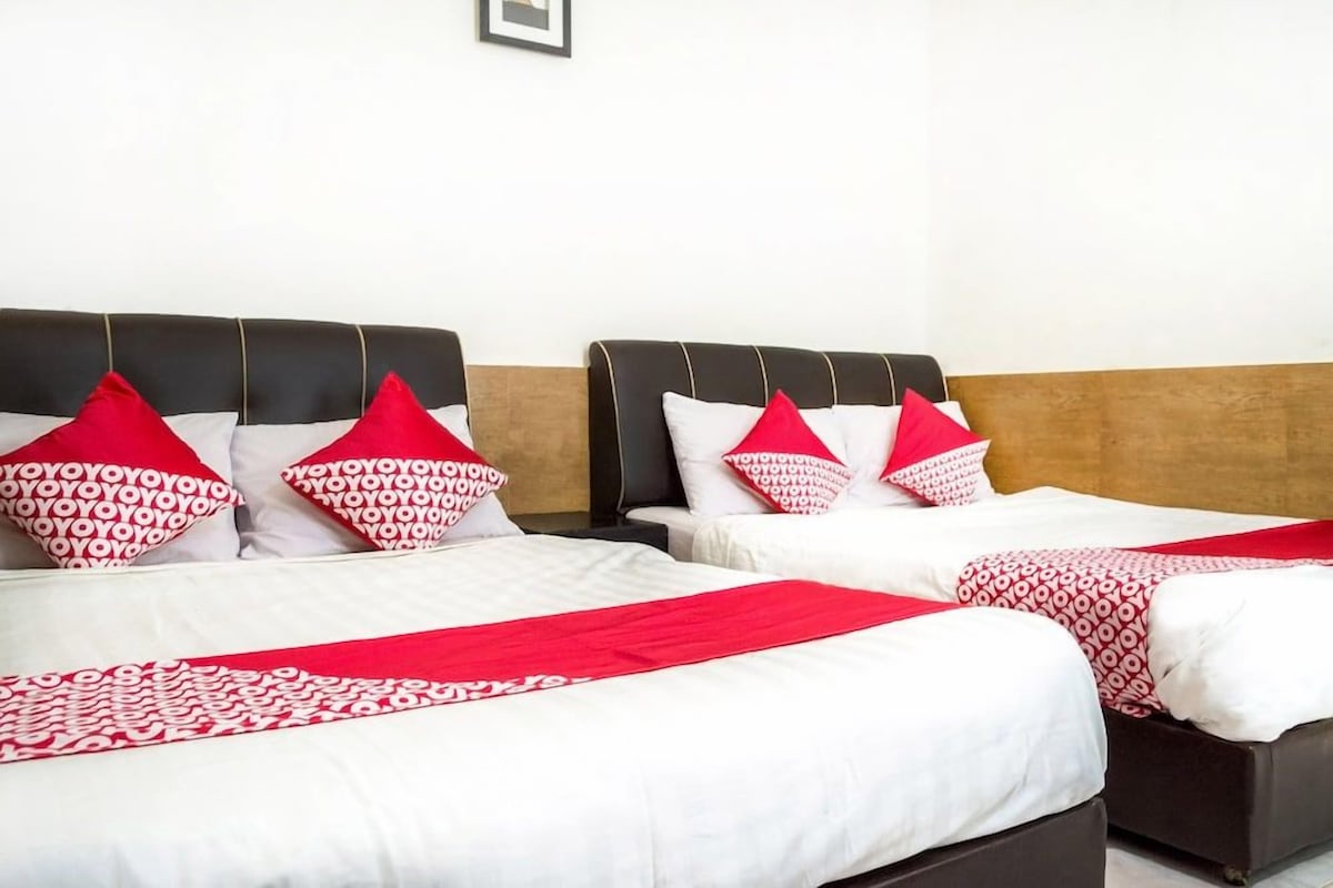 A hotel room with two beds, each with a black headboard, white bedding, and red pillows.
