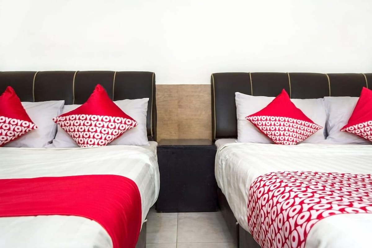 A hotel room with two beds, each with a red and white patterned bedspread and matching pillows.