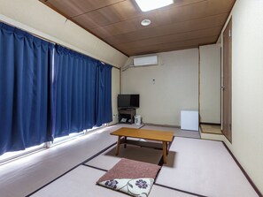 Una habitación con suelo de tatami, una mesa de madera, un televisor y un equipo de aire acondicionado blanco.