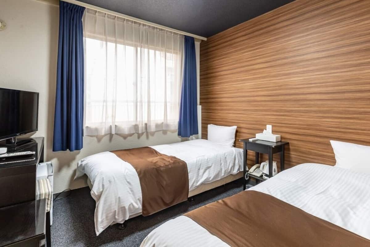 Ein Hotelzimmer mit zwei Betten, einem Fernseher, einem Schreibtisch und einem Telefon.