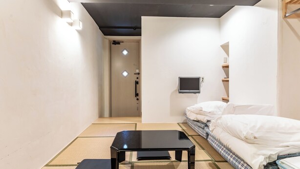 A minimalist room with tatami flooring, a black table, a bed with white bedding, and a television on the wall. - Tabist Business Hotel Japan Takamatsu Kagawa (Takamatsu)