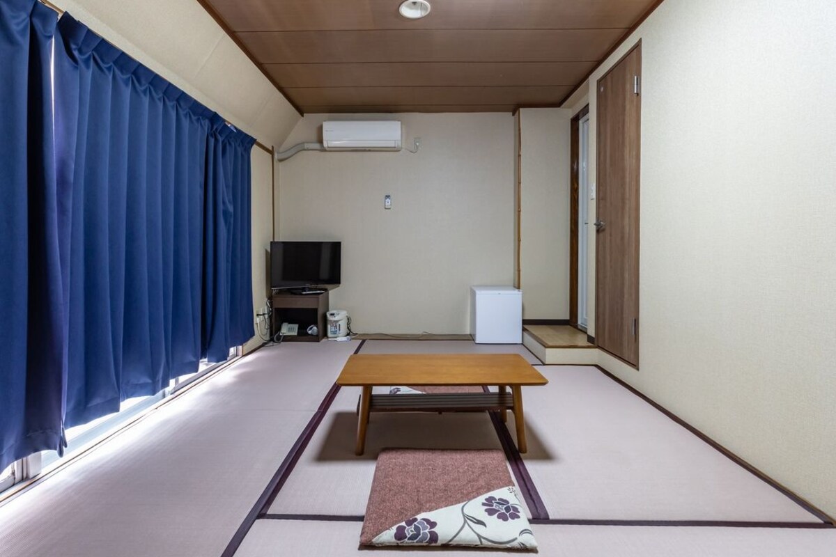 A room with tatami flooring, a wooden table, a television, and a white air conditioning unit.