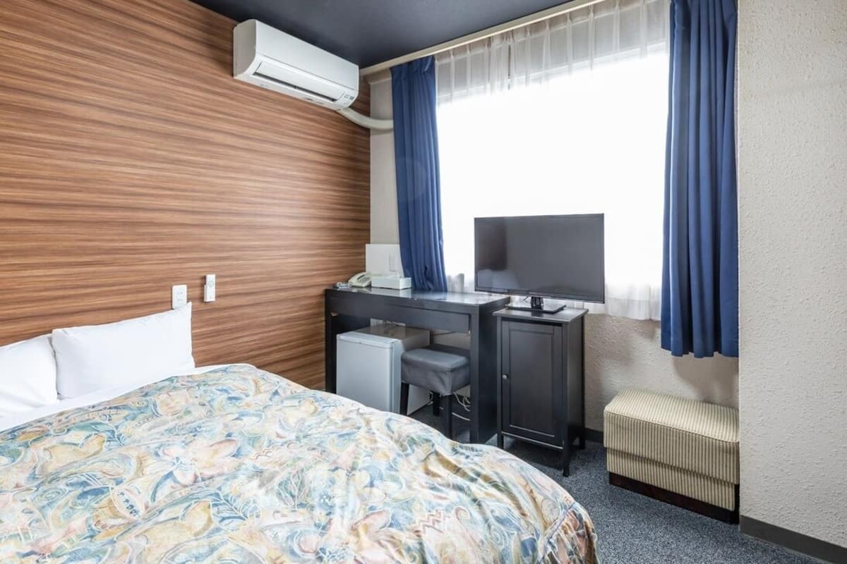 Ein Hotelzimmer mit Bett, Schreibtisch, Fernseher, Klimaanlage und einem Vorhangfenster.