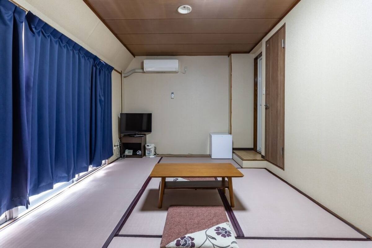 Ein Zimmer mit Tatami-Böden, einem Holztisch, einem Fernseher und einer weißen Klimaanlage.