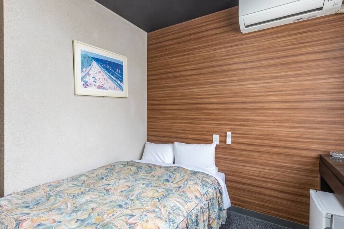 Ein Hotelzimmer mit einem Bett, einem Holzkopfteil, einem gerahmten Bild an der Wand und einer Klimaanlage.
