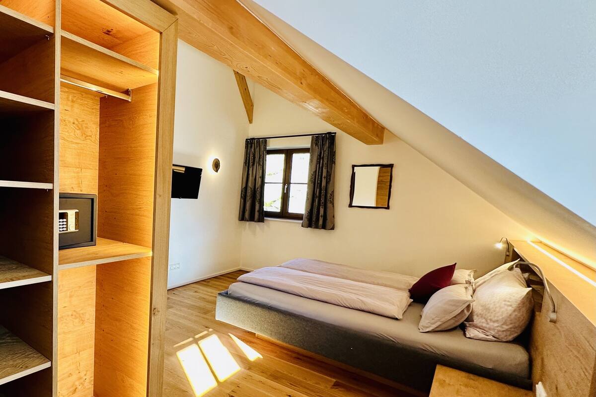 A loft-style bedroom with a loft bed, wooden shelving, and a small window with curtains.