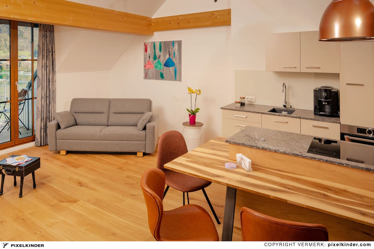 A modern kitchen with wooden cabinets, a dining table with chairs, a sofa, and a painting on the wall.