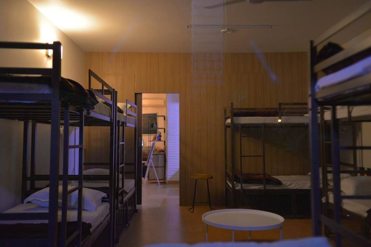A dormitory-style room with bunk beds, a small round table, and a ladder leading to a loft area.