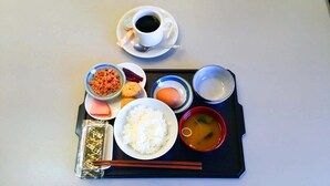 Ein Tablett mit einer Kaffeetasse, einer Reisschale, einer Suppenschale, einem Teller mit Fleisch, einer kleinen Schale eingelegtem Gemüse und einer Packung Instantnudeln.