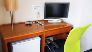 Ein Hotelzimmer mit einem Holztisch, einem Panasonic-Fernseher, einem kleinen Kühlschrank und einem leuchtend grünen Sessel.