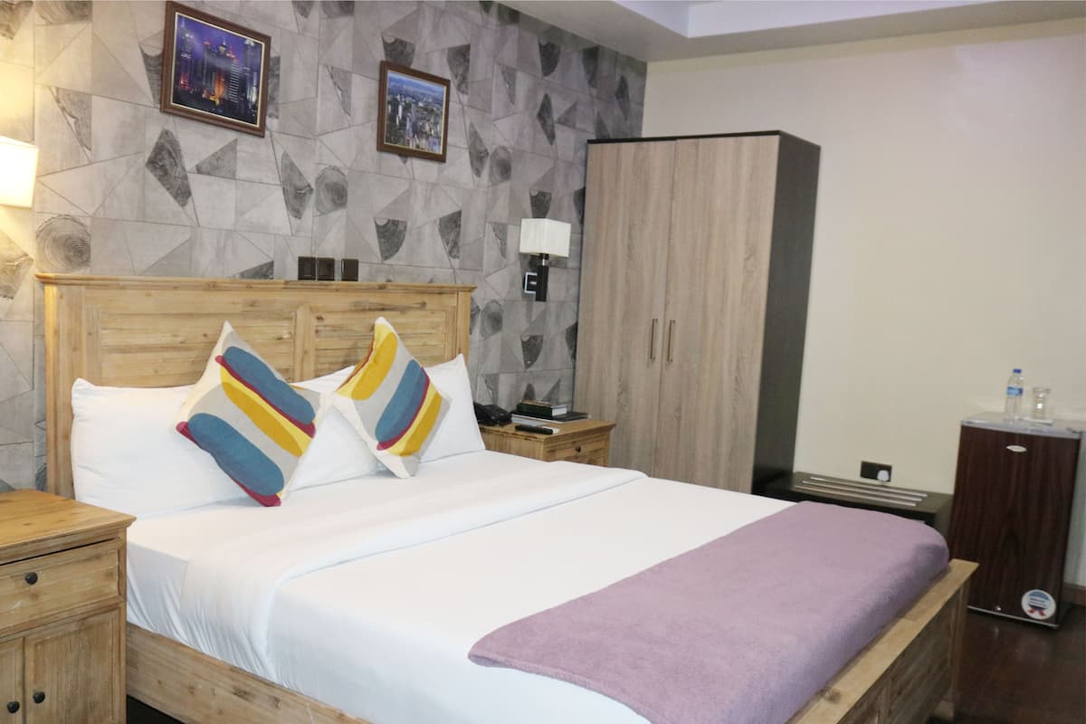 A neatly made bed with a wooden headboard, a nightstand with a lamp, a wardrobe, and a small table with a water bottle.