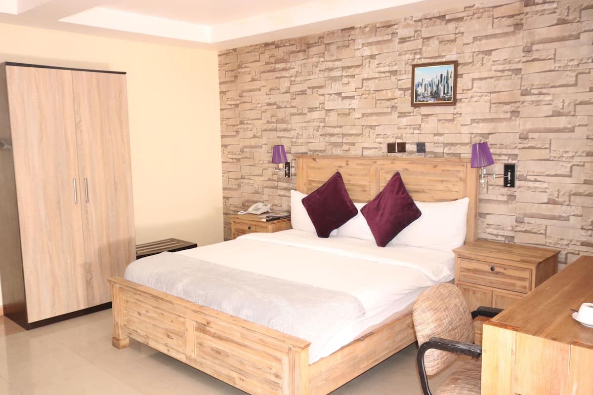 A bedroom with a wooden bed, a nightstand, a desk, a wardrobe, and a stone wall.