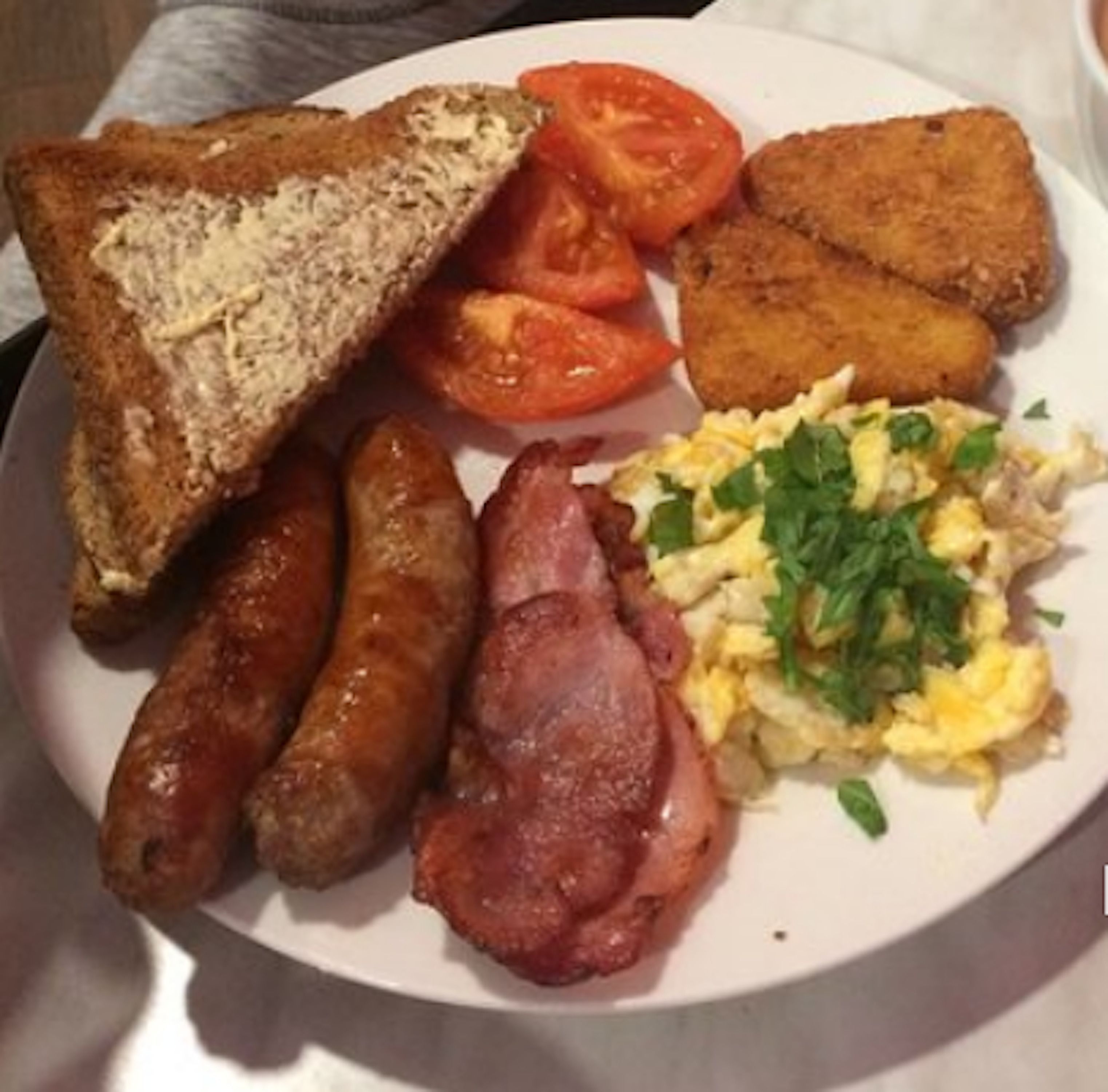 Een bord met toast, worstjes, spek, roerei en tomaten.