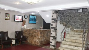 A reception area with a marble counter, two leather chairs, a television, and a clock on the wall. - Villa ToscanaHotels (Lagos)