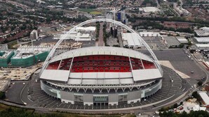 En stor stadion med en markant, bågformad konstruktion, omgiven av byggnader och vägar i stadsmiljön.