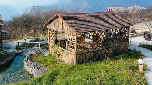 A rustic wooden structure with a tiled roof, surrounded by a stone pathway and a small water feature. - Gayane Hotel (Haghpat)