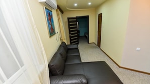A hallway with a dark brown leather sofa, a painting on the wall, and an air conditioning unit. - Gayane Hotel (Haghpat)