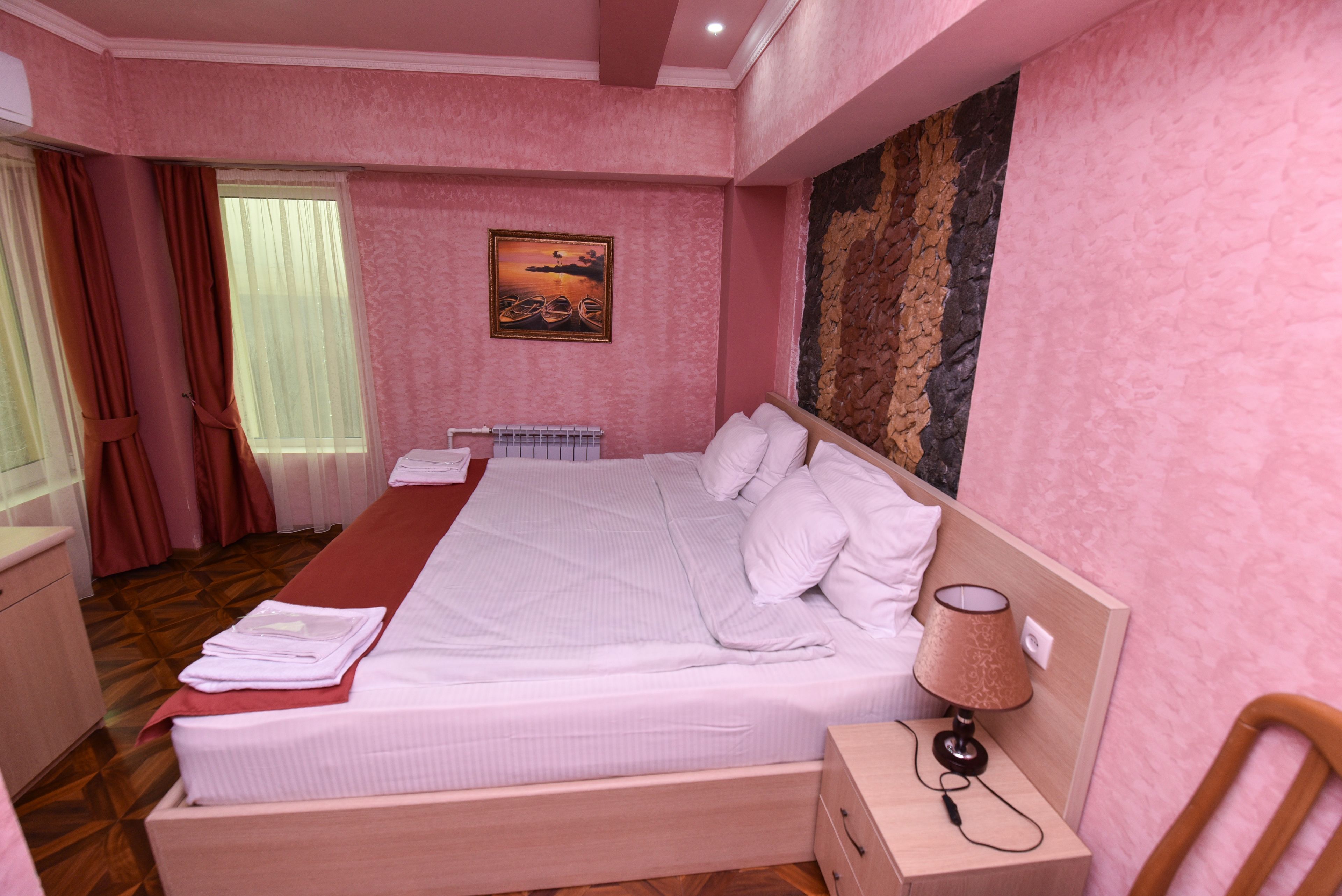 A neatly made bed with pillows and a blanket, a bedside table with a lamp, and a painting on the wall.