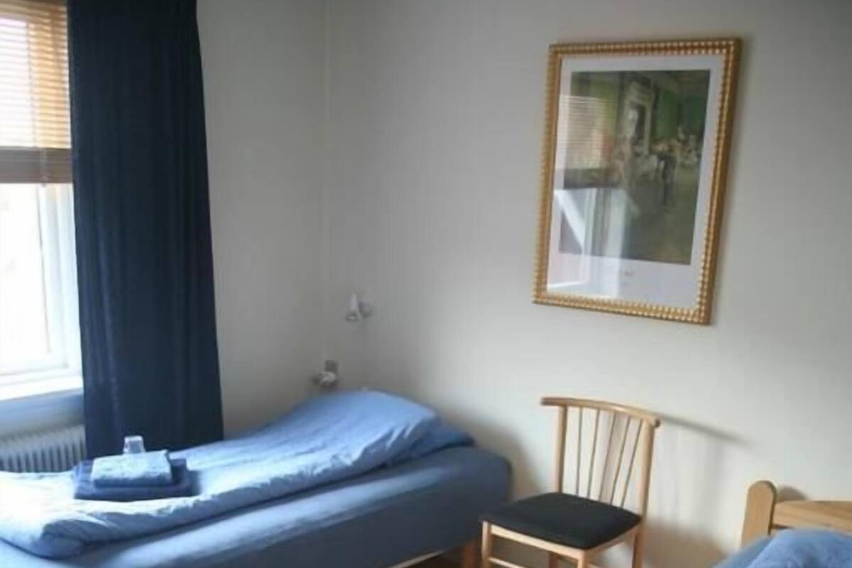 A room with two single beds, a wooden chair, a desk, and a framed picture on the wall.