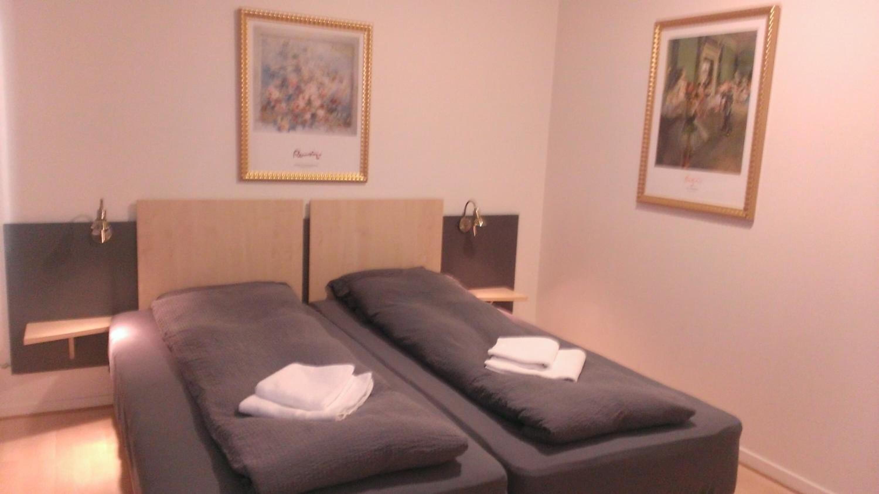 A twin room with two beds, each with a headboard and bedside tables. There are framed pictures on the walls.