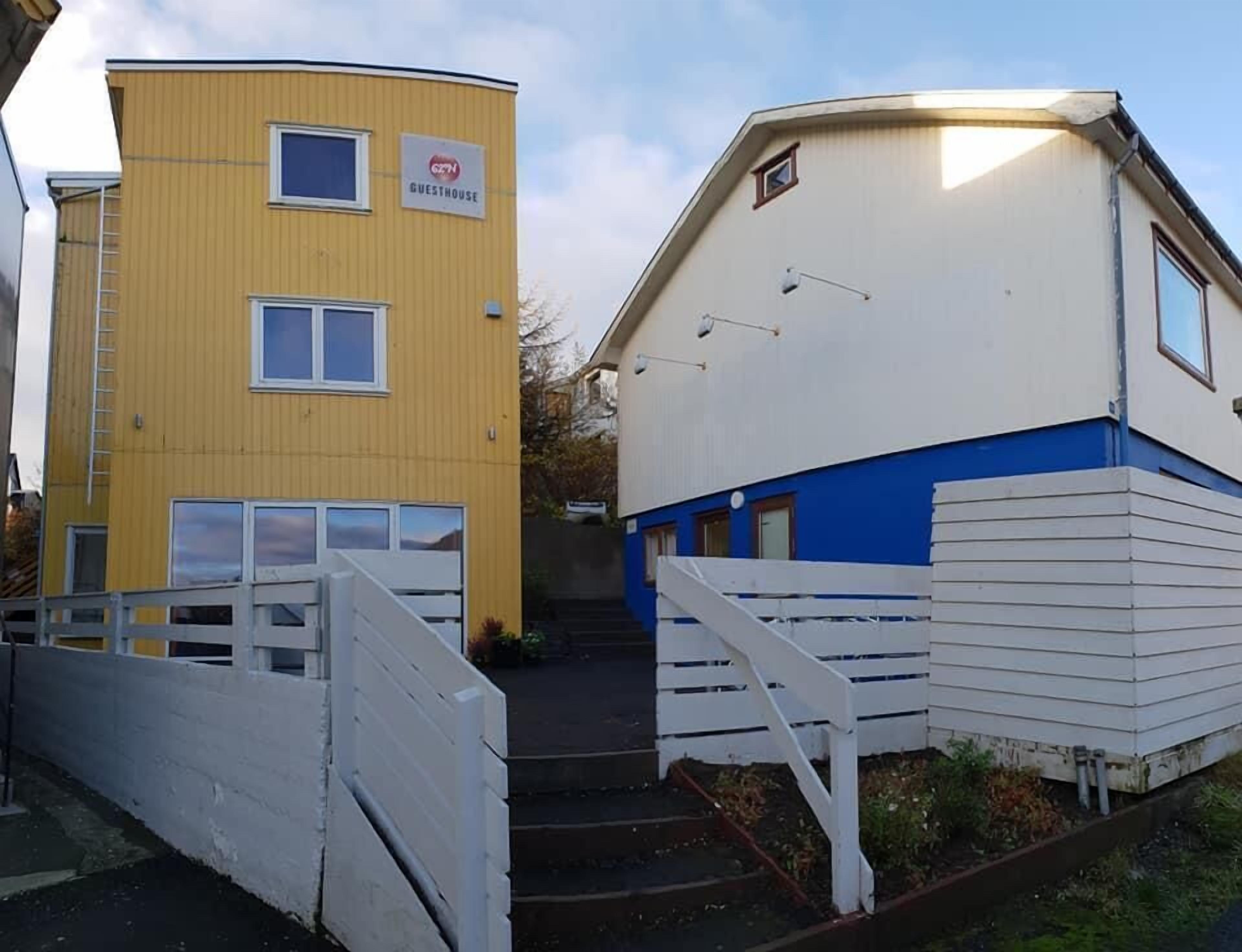 A yellow building with a sign labeled "GUESTHOUSE" and a white building with a blue section and a staircase leading to a door.