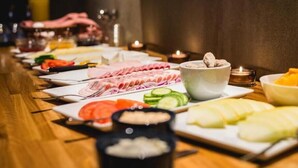 Ein langer Tisch mit verschiedenen Speisen und Beilagen, darunter Aufschnitt, Gemüse und eine Schüssel mit Pilzen.