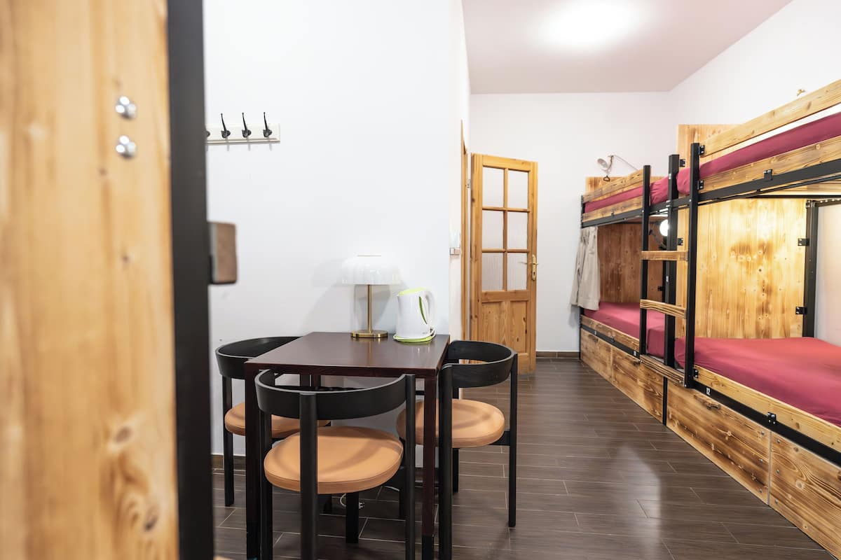 Una habitación con una cama litera de madera, una mesa de comedor con sillas y una lámpara.