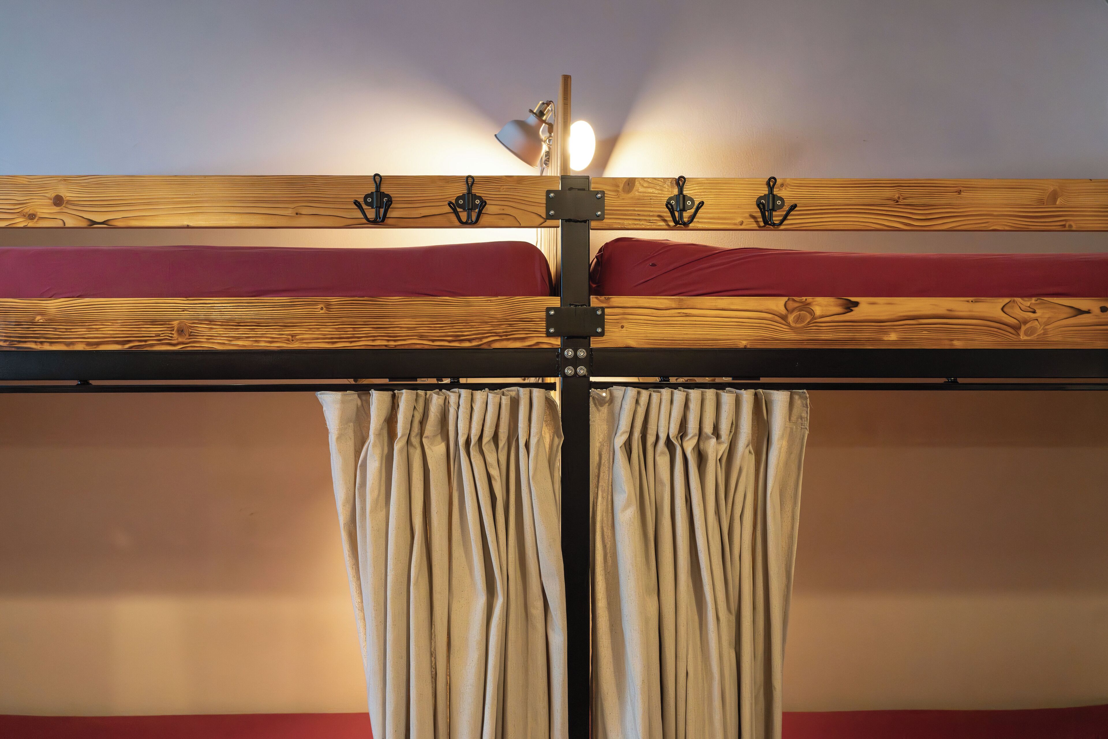 A bunk bed with a wooden frame, a red mattress, and a headboard with hooks. There is a curtain on the window.
